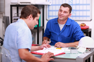 Two men sitting at a table with papers and a calculator in front of them.