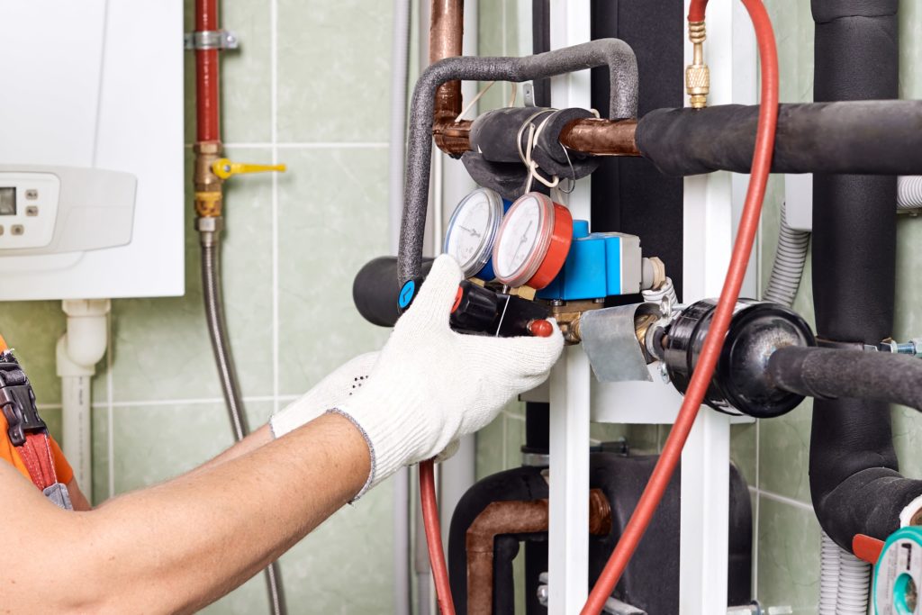 Maintenance engineer checking technical data of heating system equipment in a boiler room. Plumber installing pressure meter for house heating system.